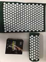 Overview of green acupuncture mat, neck pillow, and boxed 5 lb dumbbell set on white surface.