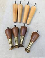 Photo showing four light wood tapered furniture legs and four dark wood legs with brass bases lying on a surface