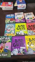 Photo shows nine children's books arranged on a dark surface. Titles include Dog Man, Cat Kid Comic Club, and The Bad Guys series, mostly by Dav Pilkey and Aaron Blabey. Covers are colorful with illustrated cartoons.