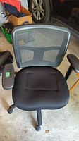 Front-facing view of the black office chair showing mesh backrest, padded seat, and armrests.