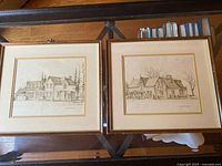 Two framed architectural house prints laid on a glass table, showing both drawings side-by-side.