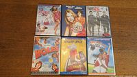 Lot of 6 comedy DVDs: 13 Going on 30, Drive Me Crazy, This Means War, Holes, Stuart Little, Bend It Like Beckham case covers arranged on wooden surface.