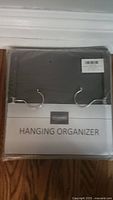 Front view of the packaged hanging organizer showing the Room Essentials label, hooks, and dark fabric inside clear plastic packaging.