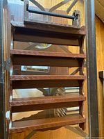 Front angled view highlighting the five shelves with carved geometric pattern on edges and top mounting bar for hanging.