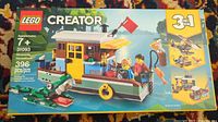 Front image of unopened Lego Creator set 31093 Riverside Houseboat box showing boat with minifigures and accessories in colorful water setting.