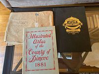 Photo displaying the two 1881 Illustrated Atlases of the County of Simcoe with their slipcase, and the large manila envelope containing the newspaper.