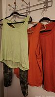 Four items of Lululemon clothing hanging on hangers: light green tank top, orange tank top, orange shirt, and patterned leggings on lower hanger.