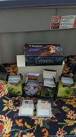 Commander Legends booster box on top and four open small boxes filled with Magic the Gathering cards arranged on a colorful patterned carpet.