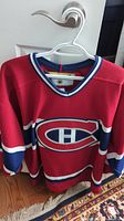 Front view of used Montreal Canadiens red hockey jersey on hanger, showing team logo and stripes.