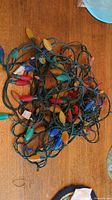 Photo of tangled string of vintage multicolored Christmas lights with large bulbs in red, yellow, blue, and orange on green wiring.