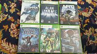 Photo of all six Xbox 360 game cases showing titles Alpha Protocol, Alan Wake, Afro Samurai, Brutal Legend, Enslaved, Bayonetta.