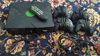 Microsoft original Xbox console with green logo on top, power and AV cables connected, accompanied by four controllers including one with damaged cable, plus Xbox DVD controller and receiver.
