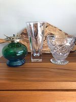 Front view of three items on wooden surface: green and blue glass oil lamp base, tall clear glass vase, and Waterford cut crystal vase