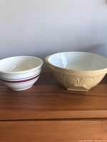 Two vintage ceramic mixing bowls side by side on a wood surface: Robinson Ransbottom bowl with burgundy and blue stripes, and a beige T.G. Green Gripstand bowl with embossed patterns.