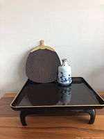 Blue hand-painted ceramic sake bottle on black lacquerware pagoda tray with black fan-shaped plate behind