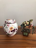 Front view of the Floris of London pot pourri jar and Asian stone bonsai plant set side by side on a wooden surface against a plain wall.