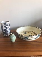 Lot of three studio pottery pieces: a Raku vase with black brushstroke pattern, a large Sandi Dunkelman bowl, and a small green vase grouped on a wooden surface