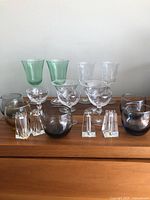 Photo showing all glassware in the lot grouped, including green water goblets, cut crystal glasses, whiskey glasses, wine glasses, and salt and pepper shakers.
