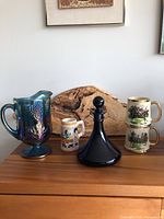 Full lot featuring a blue iridescent Harvest pitcher, steeplechase tankards, German style stein, and cobalt blue ship's decanter.