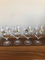 Photo showing all four Martha Stewart glass goblets with hydrangea floral decoration on a wooden surface against a plain wall.