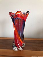 Front angled view of tall Murano glass vase showing swirling red, orange and purple colors cased in clear glass with wavy rim.