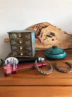 Wide view of the gold and Tiffany Blue wooden jewelry box with noticeable paint loss, two copper horseshoes, Blue Mountain Pottery turquoise trinket box with lid, and two beer taps with logos visible on handles.