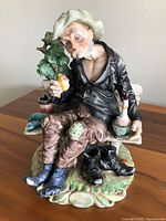 Full view of the Capodimonte porcelain figurine showing old man seated on bench with boots off and holding food.