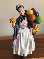 Full frontal view of Royal Doulton Biddy Penny Farthing figurine standing approximately 9 inches tall holding balloons and flowers, showing detailed handpainted dress and facial features.