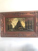 Full view of the framed cityscape painting showing the ornate wooden frame and the painted scene of a city street with a triangular building.