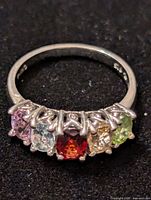 Front view of sterling silver ring showing five prong-set colored birthstones: pink, pale blue, deep red, amber, light green.