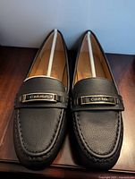 Pair of new women's black leather loafers sized 9 with Calvin Klein metal branding on front.