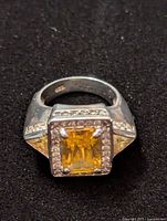 Top front view of a sterling silver ring with a square-cut citrine gemstone and surrounding small clear stones, set in a bezel.