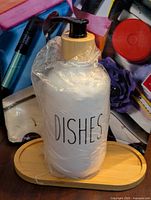 Plastic dish soap refill bottle labeled 'DISHES' with wooden pump and wooden base in use environment, plastic is still on bottle.