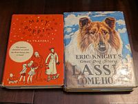 Two vintage hardcover books on a table: Mary Poppins with an orange cover, Lassie Come-Home with a dust jacket featuring a Collie dog portrait.