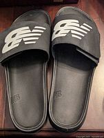 Top view of the black New Balance slides showing adjustable straps with large white 'NB' logos and contoured footbeds.