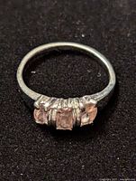 Front view of a silver ring with three pink gemstones on black background, showing the stones and prong setting.