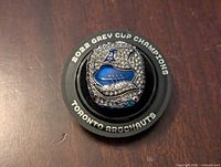 Close-up photo of the top of the replica ring with clear rhinestones and Toronto Argonauts logo in blue with black background surrounded by text '2022 GREY CUP CHAMPIONS TORONTO ARGONAUTS'.
