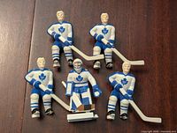 Front view of five Toronto Maple Leafs hockey figure models including four skaters and one goalie, dressed in white jerseys with blue maple leaf logos.