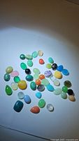 Photo showing assortment of polished cabochon gemstones in various colors and shapes under light.