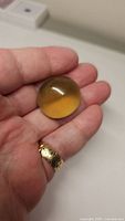 Natural oval cabochon cut lemon citrine gemstone placed on a hand showing size and smooth polished surface with yellow gradient color.
