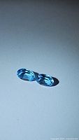 Close-up of two oval cut Swiss blue topaz gemstones on a white background showing vibrant blue color and clarity.