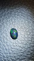 Full view of the oval black opal resting on textured dark surface showing overall size and shape.