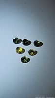 Six small round diamond-cut sapphires in greenish-yellow hues placed on a white background, showing size and color variation.