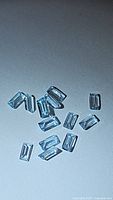 Close up image showing 13 baby blue topaz baguette cut gemstones scattered on a surface, highlighting their pale blue color and rectangular shape.