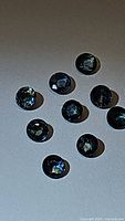 Close up of ten natural blue sapphire gemstones showing diamond cut facets and green undertones, approximately 3mm each.
