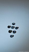 Seven natural blue sapphire gemstones arranged on a flat surface, showing round diamond cuts and varied blue color tones.