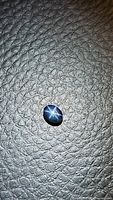 Natural blue star sapphire gemstone photographed on a dark textured surface, showing the stone's oval shape and six-ray star asterism.