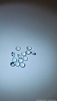 Photo of 11 loose natural round cut baby blue topaz gemstones approximately 3mm each, placed on a plain surface with light reflecting off facets.