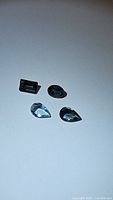 Photo showing four natural blue tourmaline gemstones in different cuts and shapes, displayed on a white background.