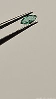 Close-up single marquis cut emerald gemstone held by tweezers showing shape, color, and clarity.